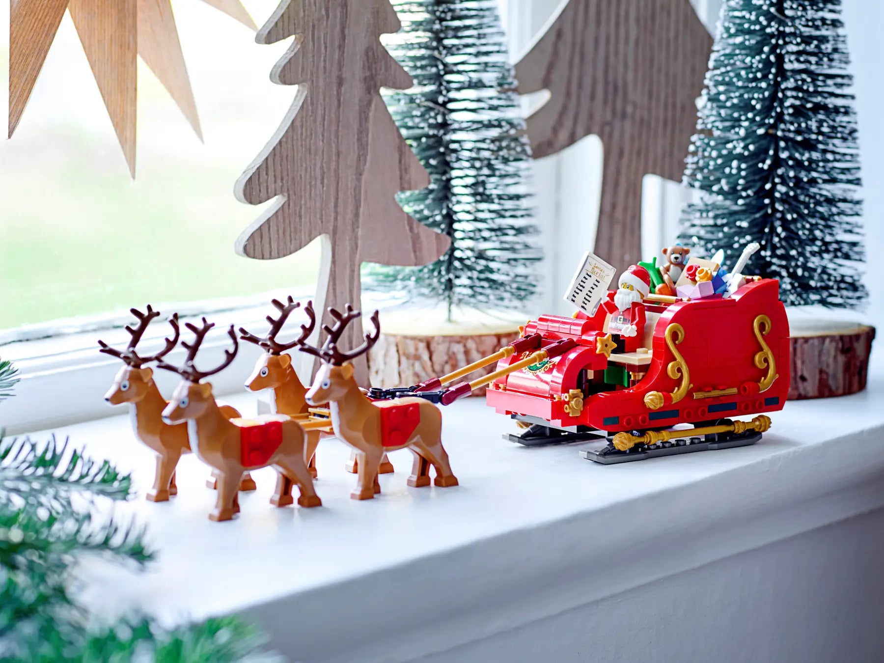 Toy Santa's sleigh with reindeer on a snowy landscape with wooden trees in the background.