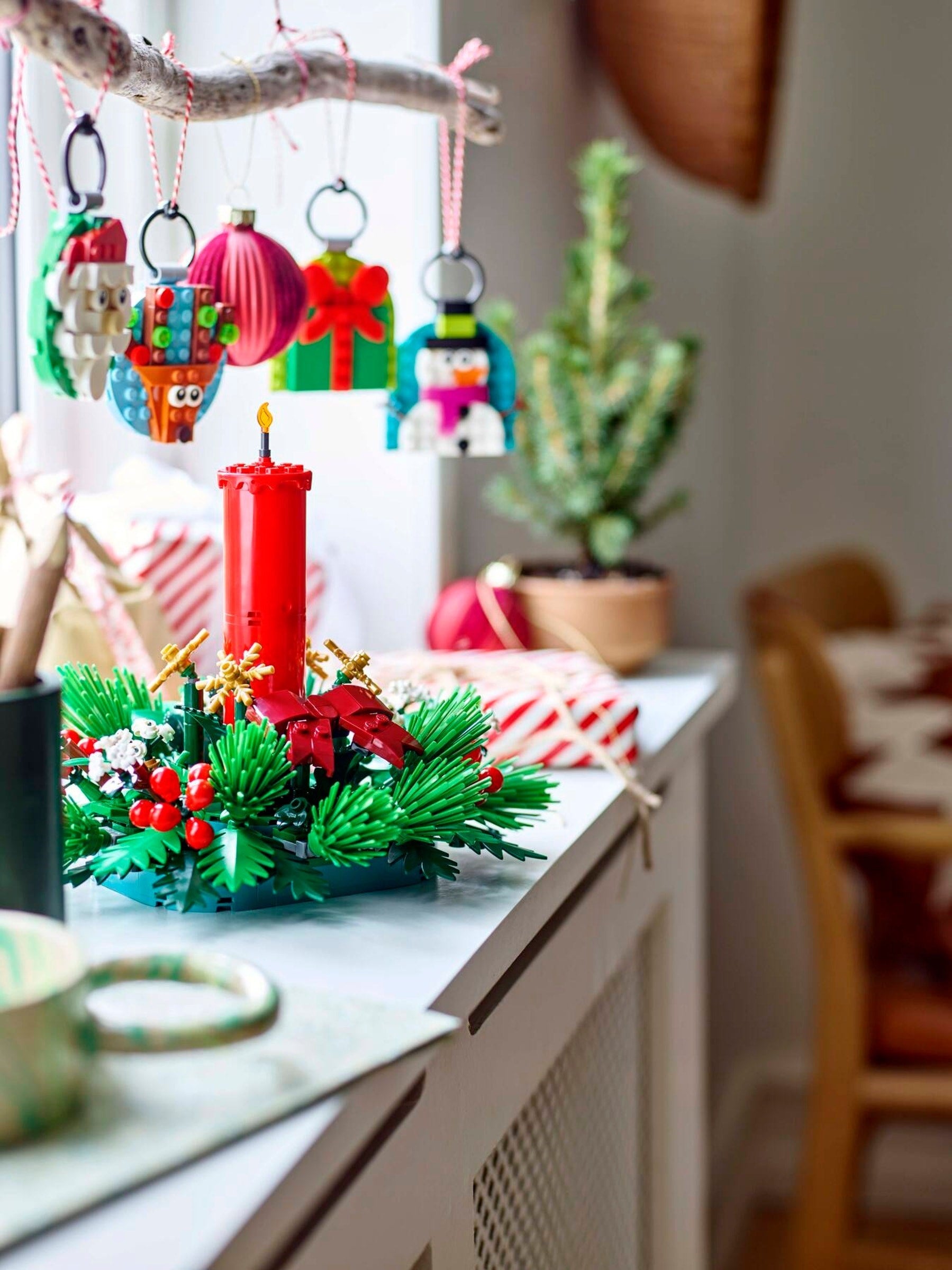 Decorative setup with colorful ornaments, a red candle, and greenery on a surface.